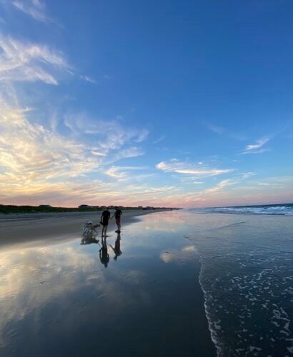 Two men walking dogs at sunset by the Atlantic Ocean in the Outer Banks, North Carolina