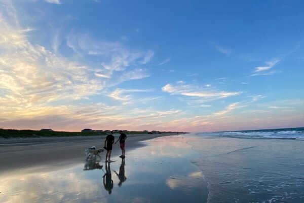 Two men walking dogs at sunset by the Atlantic Ocean in the Outer Banks, North Carolina