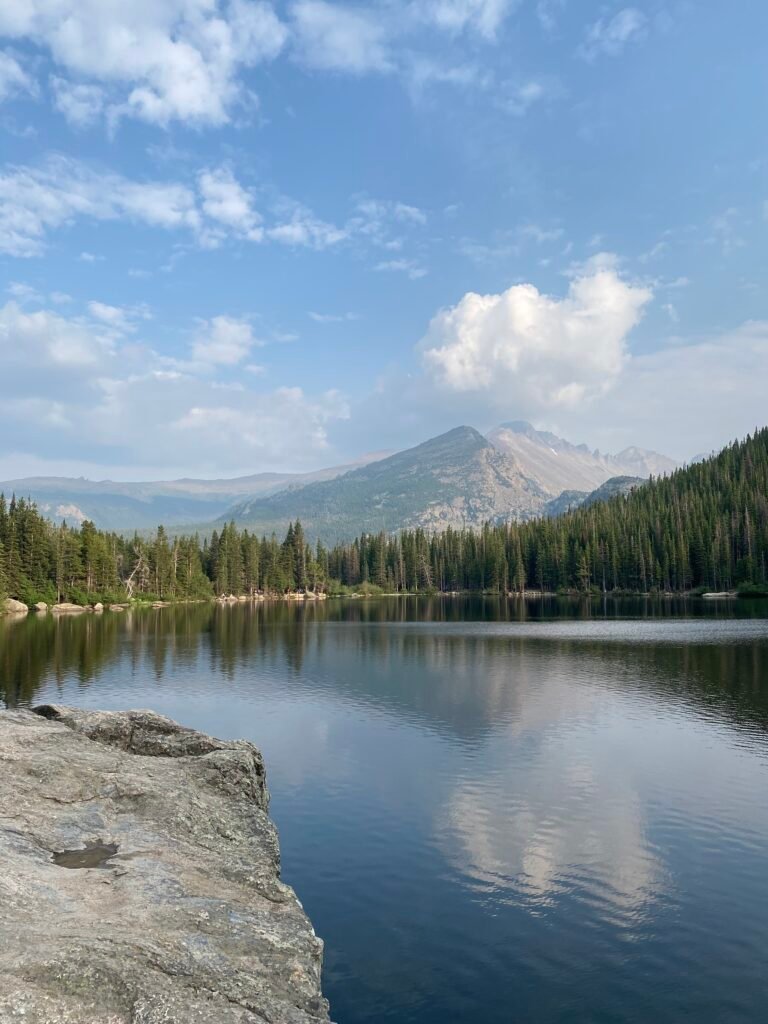 A view of an alpine lake with evergreen forest and mountains in the background in Rocky Mountain National Park, credit Big Woof Travel