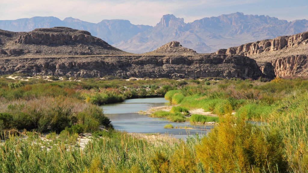 A view of the river and shrubbery at Big Bend National Park, with mountains and cliffs in the background. Credit to the National Parks Conservation Association.